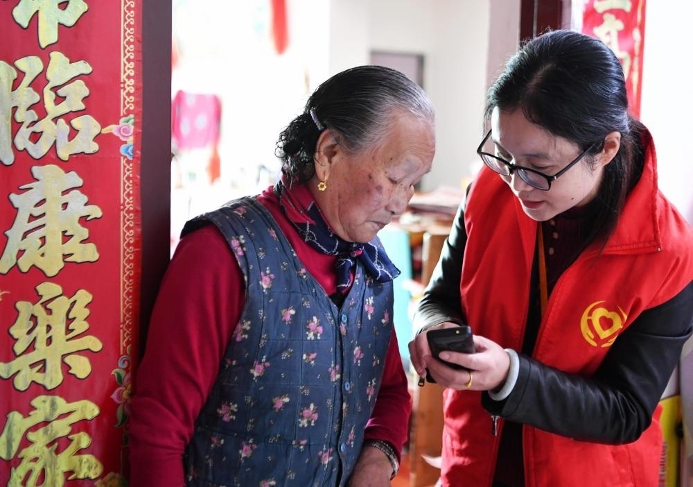 在福州市長樂區(qū)航城街道籌岐村，智慧養(yǎng)老平臺派駐社區(qū)的助老員（右）在為老人陳鳳英（左）講解養(yǎng)老定制手機的用法（2021年11月26日攝）。新華社記者 魏培全 攝