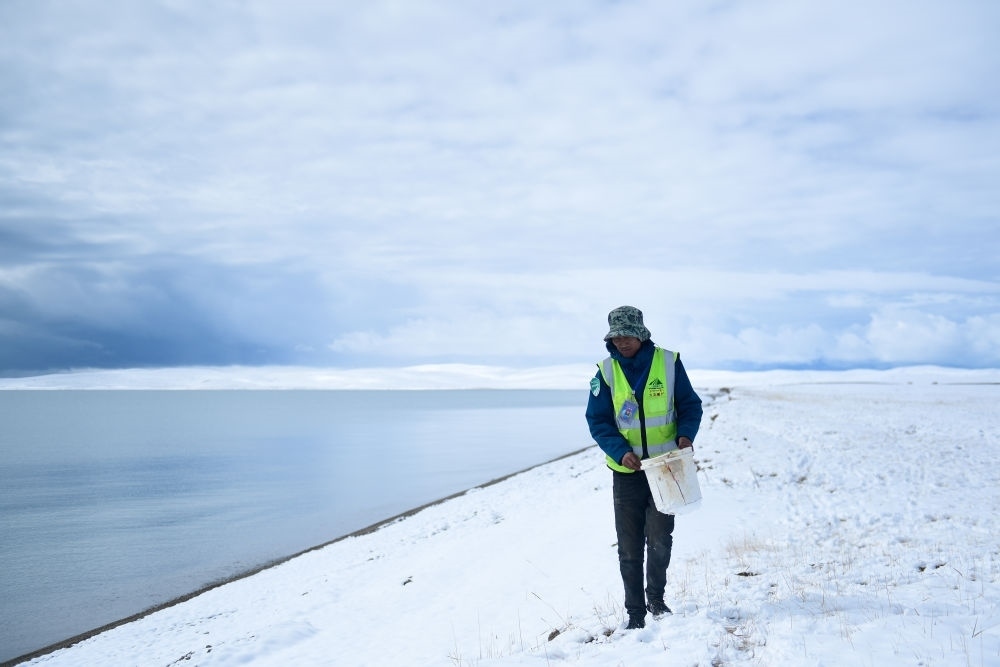 2021年10月20日，在青海省果洛藏族自治州瑪多縣扎陵湖鄉(xiāng)勒那村，三江源國家公園黃河源園區(qū)生態(tài)管護(hù)員在扎陵湖邊撿拾垃圾。新華社記者 張龍 攝