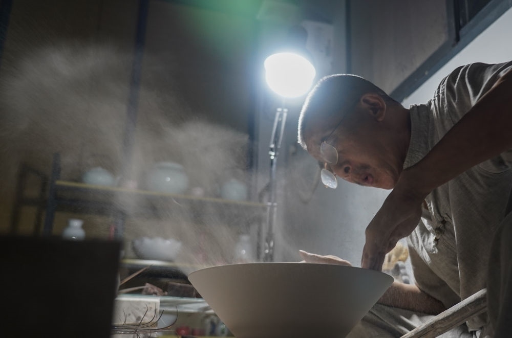 ↑ 在景德鎮(zhèn)，手工匠人吹去坯內(nèi)的泥土（2021年7月14日攝）。