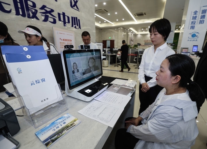 在浙江省嘉興市秀洲區(qū)王江涇鎮(zhèn)便民服務(wù)中心的“跨域通辦·云綜窗”窗口，辦理開業(yè)登記的個(gè)體工商戶（右一）通過該系統(tǒng)與江蘇省蘇州市吳江區(qū)盛澤鎮(zhèn)行政審批局工作人員視頻連線，進(jìn)行身份讀取及材料線上審核（2024年5月9日攝）。新華社記者 徐昱 攝