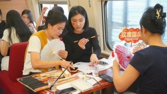 10月1日，旅客們?cè)贕1634次列車上給油紙傘作畫(huà)。新華社記者周義 攝