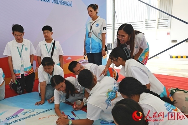 泰國學(xué)生在開營儀式展板上繪制圖案。人民網(wǎng)記者 白元琪攝