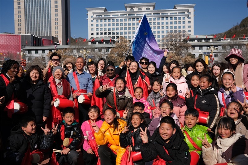 中外青年學(xué)子在安塞文化廣場觀看陜北腰鼓和大秧歌表演后合影留念，大家踏著鼓點共舞，翻飛的紅綢與躍動的身影交織，在黃土地廣場上繪出一幅生動的陜北民俗互動畫卷